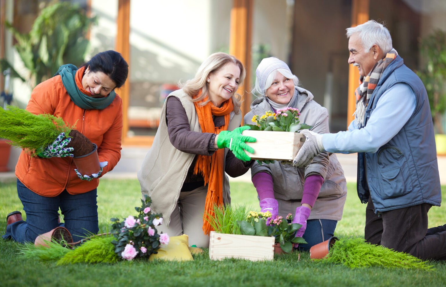 Senior friends gardening together in front of their retirement community house.